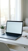 Laptop with blank screen on white desk by window with potted plant and eyeglasses, bright natural light workspace for remote work, business, or design mockup.