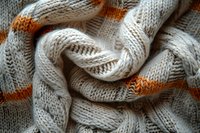 Cozy knitted fabric texture with white wool yarn and orange stripe pattern creates soft waves and folds, showing detailed stitch structure and textile warmth.