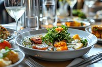Fresh salad with grilled vegetables, kale and citrus segments served in gray ceramic bowl at upscale restaurant setting with wine glass and elegant tableware.