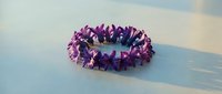 Purple crystal crown or wreath with pointed amethyst-like formations arranged in circular pattern on soft blue surface for spiritual and decorative purposes.