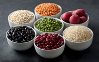 White ceramic bowls with variety of raw legumes, grains and potatoes on dark background. Collection of healthy ingredients including rice, beans, peas and lentils.