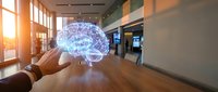 Hand holding glowing digital brain hologram in modern office space representing artificial intelligence and neural network technology for business innovation.