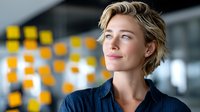 Professional young Caucasian businesswoman with short blonde hair looking confidently ahead in modern office environment with colorful background elements.