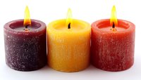 Burning aromatic candles in burgundy, yellow and orange colors arranged in row on white background, glowing wicks create cozy atmosphere for relaxation and meditation.