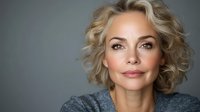 Confident mature blonde woman with curly hair smiling warmly at camera against neutral background for business and lifestyle content.