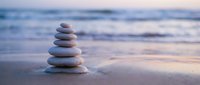 Zen stone stack on sandy beach at sunset with soft ocean waves creating peaceful meditation and mindfulness concept for wellness and spiritual balance.
