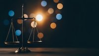 Golden scales of justice on wooden surface with warm bokeh lights creating dramatic legal concept for law firm branding and courtroom presentations.