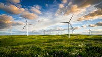 Wind turbines generating clean renewable energy on green meadow under dramatic sunset sky with golden clouds for sustainable power concepts.