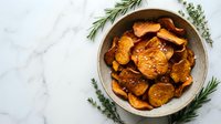 Crispy baked sweet potato chips seasoned with herbs in rustic bowl on marble surface, healthy snack alternative for cooking and nutrition content.