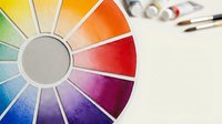 Watercolor paint palette wheel showing vibrant rainbow colors with artist brushes in background for creative art projects and color mixing techniques.