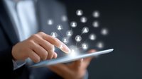 Professional in business suit holds digital tablet with glowing network of people icons floating above, representing digital connectivity and social networking.