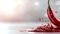 Red hot chili pepper splashing in liquid with droplets and dynamic motion effect against light blurred background, dramatic food photography concept.