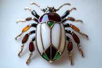 Decorative beetle brooch with mother of pearl inlay and colored enamel details on white background, vintage style jewelry design featuring geometric patterns.