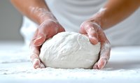 Hands kneading fresh white dough on floured surface, close-up view showing flour-covered fingers and soft elastic bread dough texture in home kitchen.