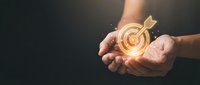 Hands holding a glowing golden target with arrow, symbolizing goal achievement, business strategy, and success in dark background.