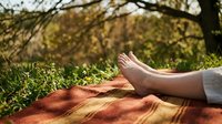 Woman relaxing barefoot on blanket in sunny park during autumn season. Peaceful outdoor leisure time for wellness and mindfulness concepts.