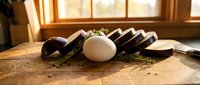 Fresh eggplant slices and whole egg arranged on rustic wooden cutting board in warm sunlit kitchen setting for healthy cooking and meal preparation.