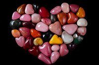 Colorful polished gemstones arranged in heart shape on black background for jewelry making, crystal healing and decorative crafts.