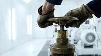 Industrial worker operating heavy machinery valve in manufacturing facility wearing protective gloves for safety protocols and equipment maintenance procedures.