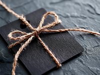 Black gift box wrapped with rustic twine bow on dark stone background, creating minimalist elegant composition for special occasions and celebrations.