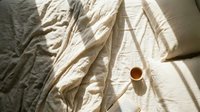 Overhead view of unmade bed with crumpled beige linen sheets and a cup of coffee, ideal for lifestyle and morning routine content.
