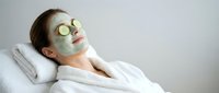 Woman relaxing with green facial mask and cucumber slices on eyes during spa treatment. Self-care skincare routine for healthy glowing skin rejuvenation.