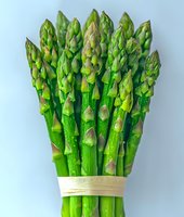 Fresh green asparagus spears bundled together with natural twine against light background, showing vibrant color and texture of seasonal vegetables.