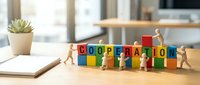 Wooden figurines arranging colorful blocks spelling cooperation on office desk with notebook and succulent plant, representing teamwork and business collaboration.