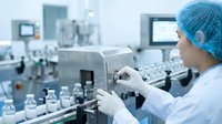 Female scientist in blue surgical cap operating automated laboratory equipment for pharmaceutical quality control testing in sterile manufacturing facility.