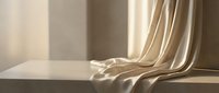 Elegant beige silk fabric draping gracefully over white surface with soft natural lighting creating luxurious textile display for interior design concepts.