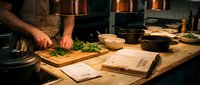 Professional chef preparing fresh herbs on wooden cutting board in modern restaurant kitchen with copper cookware and recipe books.