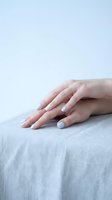 Female hands with light blue nail polish resting on soft gray fabric surface. Minimalist beauty and self-care concept for wellness and relaxation themes.