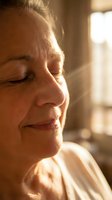 Mature woman with closed eyes in warm sunlight, profile view showing peaceful expression and natural skin texture with age-related features, suitable for wellness and mindfulness content.