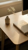 Minimalist wooden desk with dried flowers in ceramic vase, notebook, and monitor in warm natural light, evoking calm workspace.