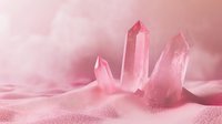 Rose quartz crystals on pink sand background with soft dreamy lighting, creating mystical healing atmosphere for wellness and spiritual concepts.