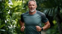 Mature athletic Caucasian male with gray beard jogging outdoors in green t-shirt, smiling while exercising against tropical foliage background in morning light.