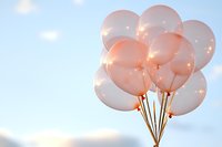 Soft pink balloons against blue sky with sunlight creating dreamy, romantic atmosphere. Party decoration for celebrations and special occasions.