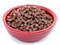Milk chocolate chips in bright red ceramic bowl against white background, isolated baking ingredient for cookies and desserts, ready for cooking preparation.