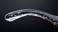 Curved stream of clear water with floating droplets and bubbles captured in high-speed macro photography against dark background, showcasing liquid dynamics.