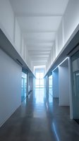 Modern office corridor with glass walls and polished concrete floors leading to bright window. Clean architectural design for corporate environments.