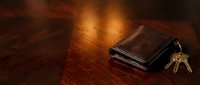 Worn leather wallet with brass keys on wooden surface, warm lighting, suitable for finance, security, and lifestyle concepts.