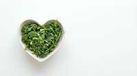 Fresh green arugula leaves in heart-shaped white bowl on clean background for healthy eating and nutrition concepts.