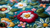 Vibrant floral embroidery pattern on teal fabric featuring red and white daisies with yellow centers, detailed leaves and mixed blooms in traditional folk style.
