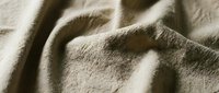 Closeup of natural linen fabric with soft folds and wrinkles, showcasing texture and neutral beige tone for textile, fashion, and interior design projects.
