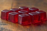 Red translucent jelly cubes arranged in rows on wooden surface with soft lighting and shallow depth of field creating appetizing dessert composition.