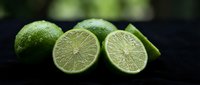 Fresh green limes whole and sliced showing juicy citrus flesh on dark surface for cooking cocktails and culinary recipes in kitchen food photography.