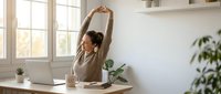 Young woman stretching arms above head while working from home office desk with laptop, taking wellness break during remote work day.