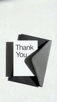 Thank you card with dark gray envelope on white textured surface, minimal style with bold typography and natural shadows.