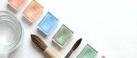 Watercolor paint palette with colorful squares and brushes arranged on white background for artistic projects and creative design work.
