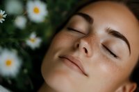 Peaceful young woman with closed eyes relaxing in nature surrounded by white daisy flowers, natural skincare and wellness concept for spa treatments.